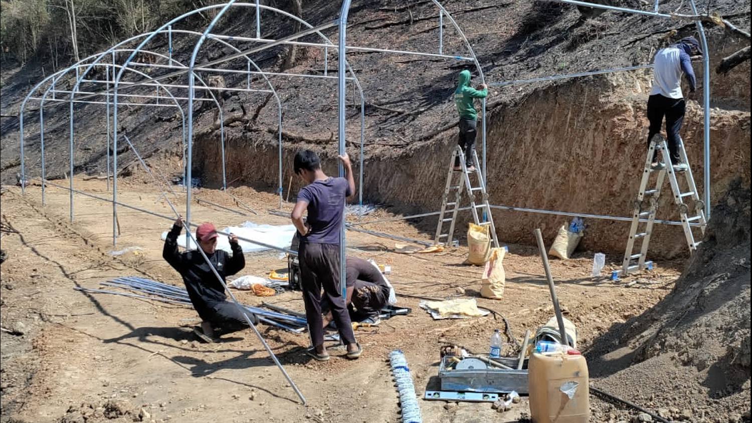 Crew assembling a galvanised steel polyhouse frame on a hillside